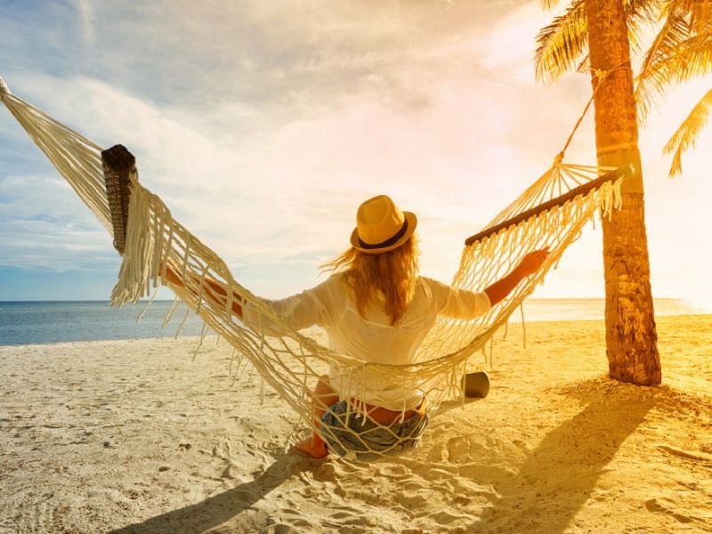 Frau mit Hut sitzt in Hängematte am Strand und schaut auf den Sonnenuntergang, Sommerloch fürs Business nutzen, Frauen im Business