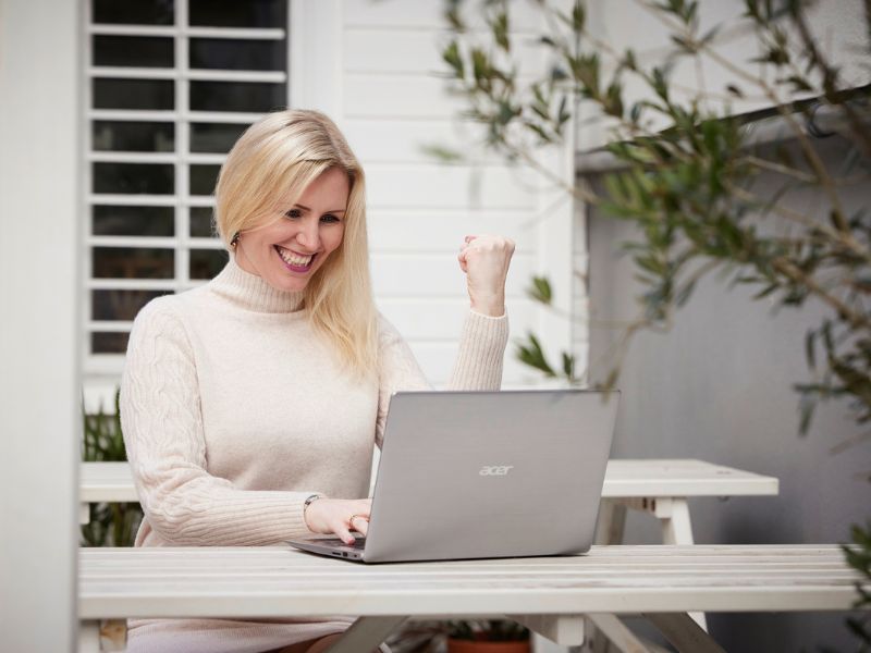 Verkaufen mit Leichtigkeit, Businesstipps, Frauen im Business, Julia Ritter ballt die Hand zur Faust und lacht, sitzend vor dem Laptop, Yes Pose einer Frau mit Laptop