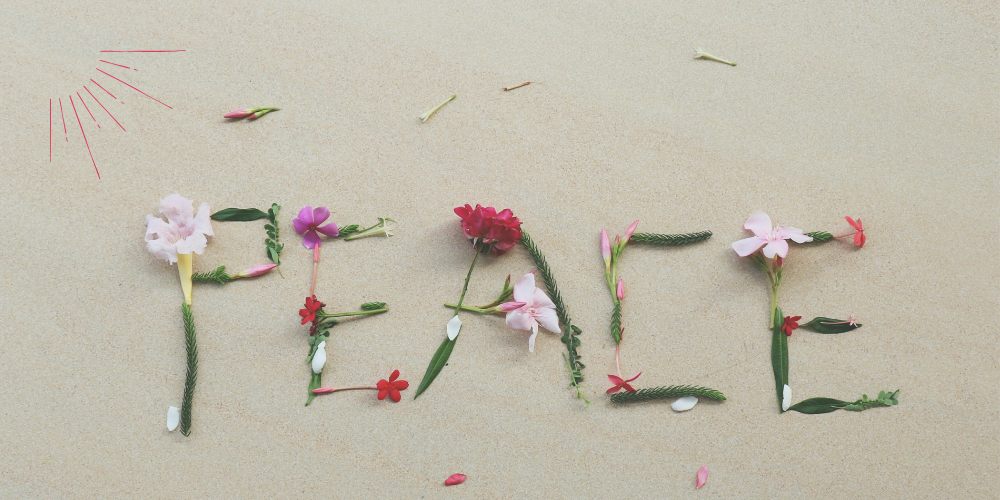 das Wort Peace, aus Blumen und Pflanzen gelegt, im Sand, vergeben, verzeihen, heilen